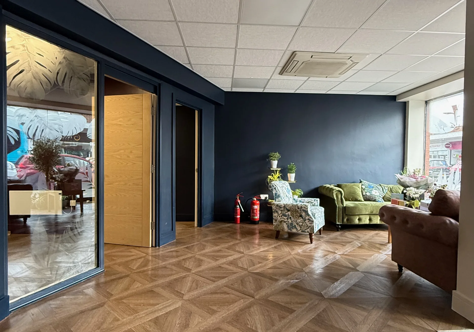 The reception area at The Wellness Lounge Leeds with green and brown sofas against a navy wall and parquet floor